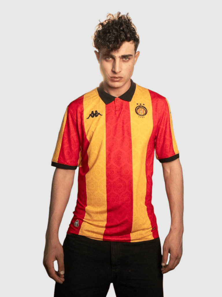 Joueur portant le Home Kit Espérance 25-26 Stadium Edition rouge et jaune sur le terrain.